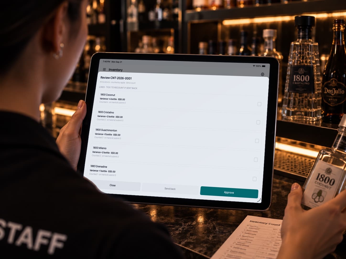 A staff member holding the iPad in front of a fully stocked shelf, reviewing a stock count